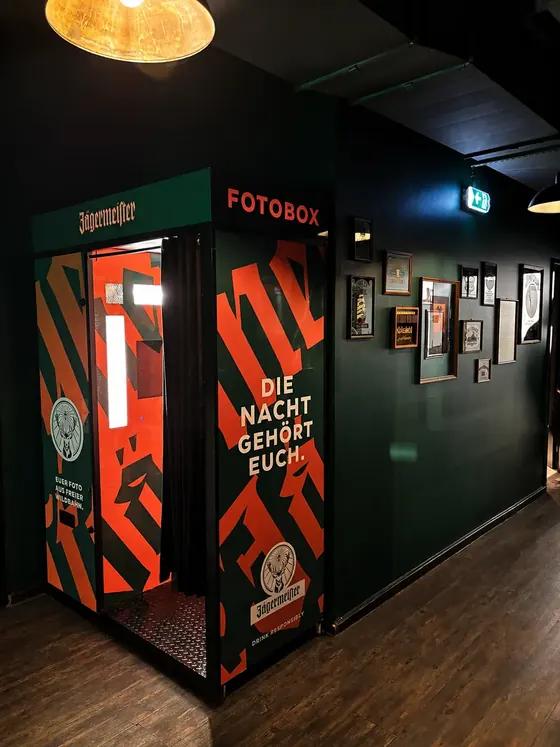 Grün-orange folierter Fotoautomat im Jägermeister-Design in einem dunkelgrünen Pub in Berlin.